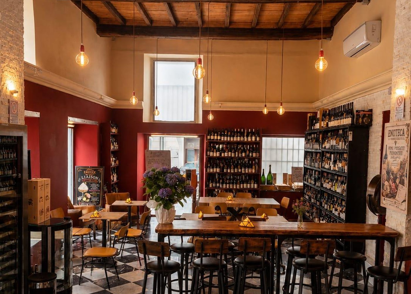 Il tavolo sociale dell'enoteca con gli sgabelli, sotto le travi a vista e le lampadine Edison